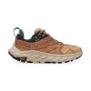 A side view of a tan and black athletic shoe, sustainably crafted for the day-hiker, with a thick beige sole and a Vibram logo. The product is the HOKA ONE ONE ANACAPA LOW GTX TIGER'S EYE/BLACK - MENS by Hoka.