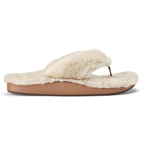 A side view of a beige, furry flip-flop sandal with shearling-wrapped straps and a cushioned sole. It features an anatomical PU footbed and has a flat brown base. This is the OLUKAI KIPE'A HEU TAPA - WOMENS by Olukai.