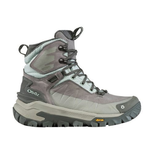 A gray and light green Oboz OBOZ BANGTAIL MID INSULATED BDRY WINTER QUARTZ - WOMENS hiking boot with a rugged Vibram Arctic Grip sole, metal eyelets, and sturdy laces designed for outdoor trekking.