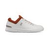 A white athletic shoe inspired by tennis style, featuring a red-brown inner lining and sole. The ON THE RODGER ADVANTAGE WHITE/RUST - MENS by On Running has a minimalist design with small perforations and a logo on the side, ideal for those seeking casual style akin to Roger Federer’s classic look.